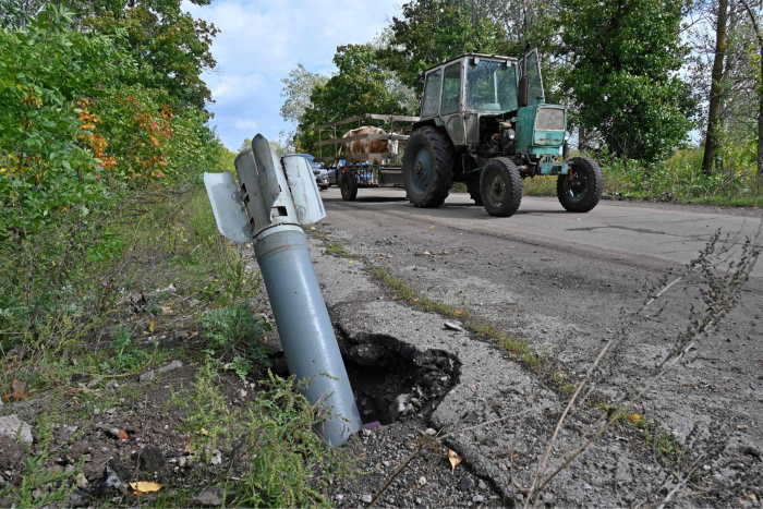 On a country road, a tractor drives past a missile that has plunged into the roadside