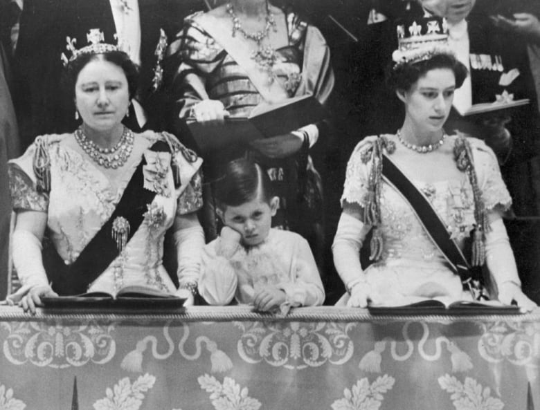 A child leans on his hand as he stands between two adults.