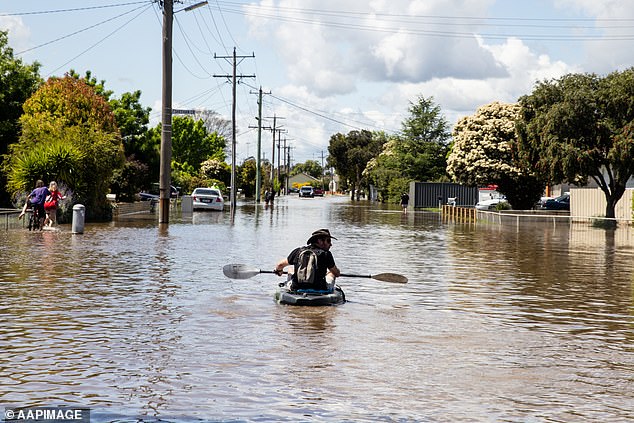 More than 350 roads are expected to remain closed in Victoria's flood-affected areas and about 6000 properties are without power (pictured, a resident paddles through Shepparton)