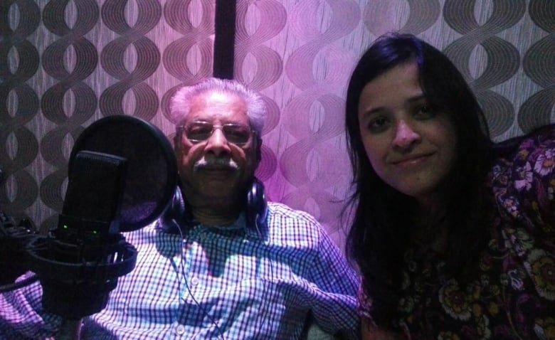 A woman leans in next to an older man in a recording booth.