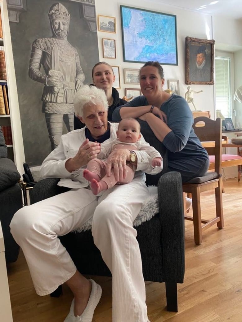 A woman with white hair sitting in a chair and holding a baby. She’s surrounded by other women.