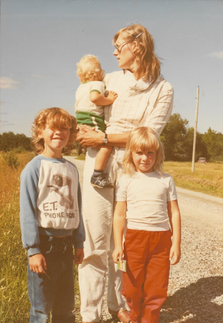 A woman holds a child in her arm while two other children stand close to her.