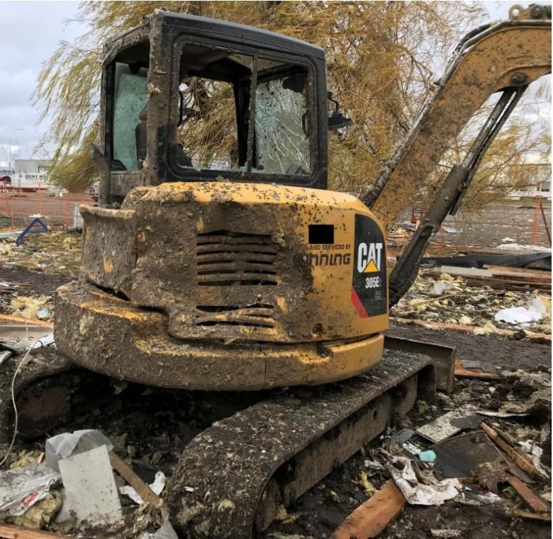 A CAT excavator is shown with its windows blown out and significant damage.