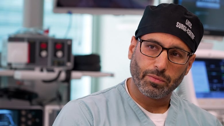 Bearded man wearing hospital scrubs and an OR cap.