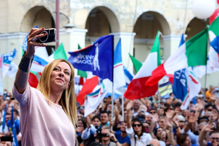 Giorgia Meloni takes a selfie on a mobile phone with a crowd of supporters behind her