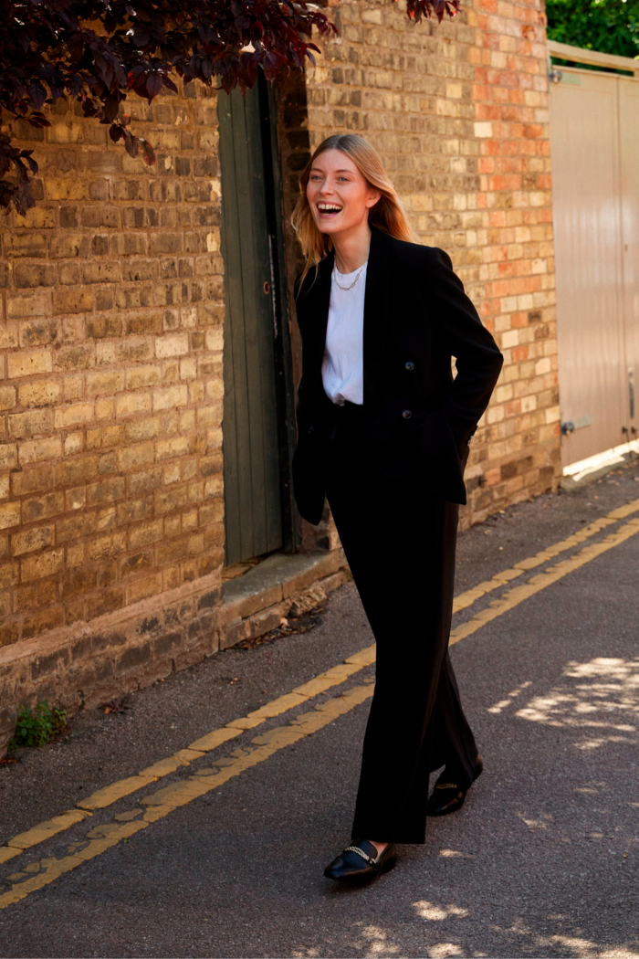 A female model walks along an autumnal street in a trouser suit