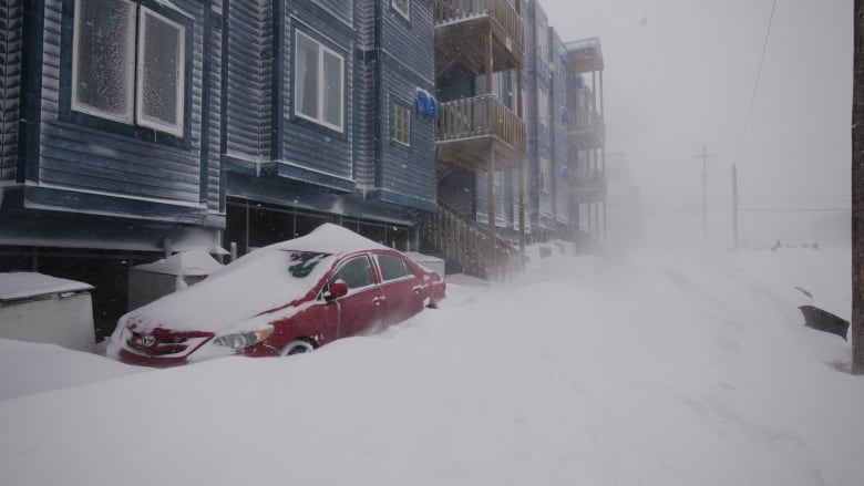 A car partially buried in snow during a blizzard.