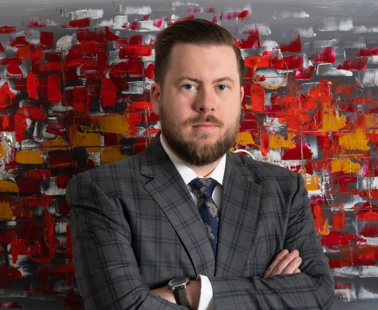 A portrait of a man in a grey suit with his arms folded.