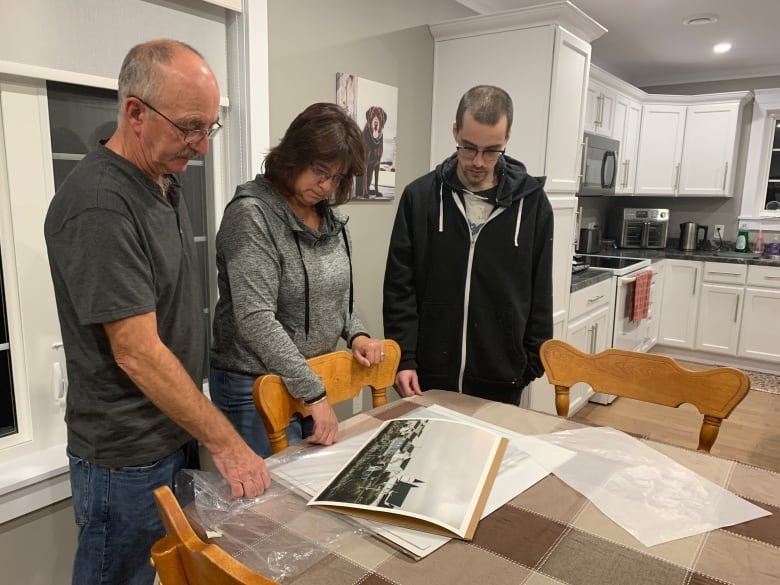 A family gathers around a print on a dining room table