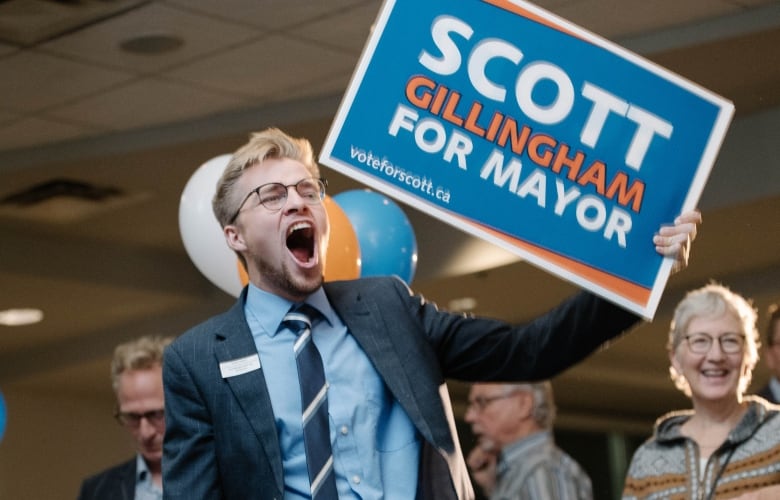 A young man in a tie holding a Scott Gillingham sign cheers.