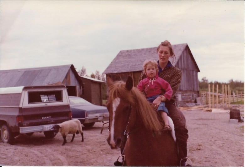 A woman and child on horseback in a farm.