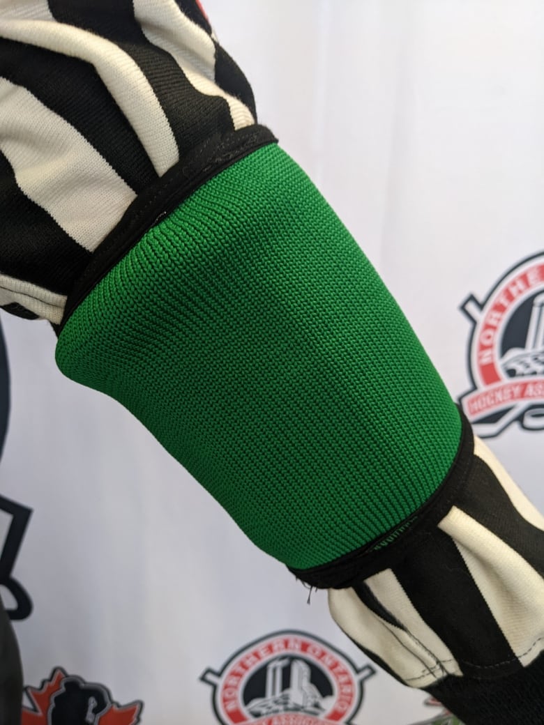 A referee's arm with a green armband around the black and white shirt.