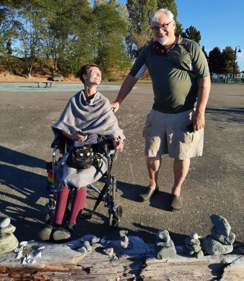 A woman in a wheelchair smiles up at a man laughing beside her.