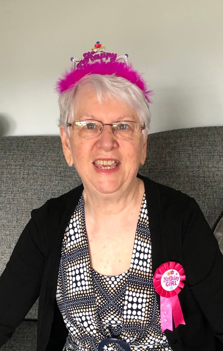 An older woman is smiling. She wears both a birthday headpiece and ribbon.