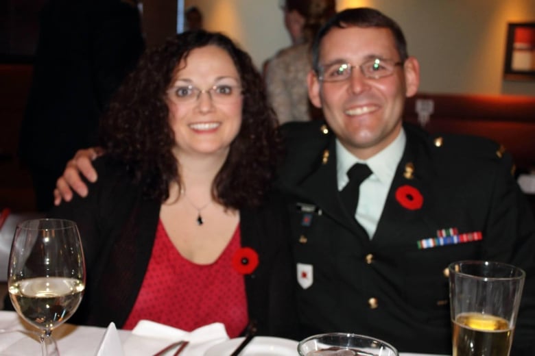 A smiling woman in civilian clothes and a man in a regimental uniform seated at a dinner table. Both are wearing poppies.