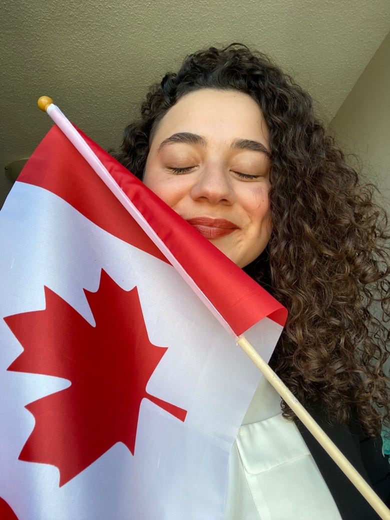 A woman closes her eyes and smiles while she holds a Canadian flag. 