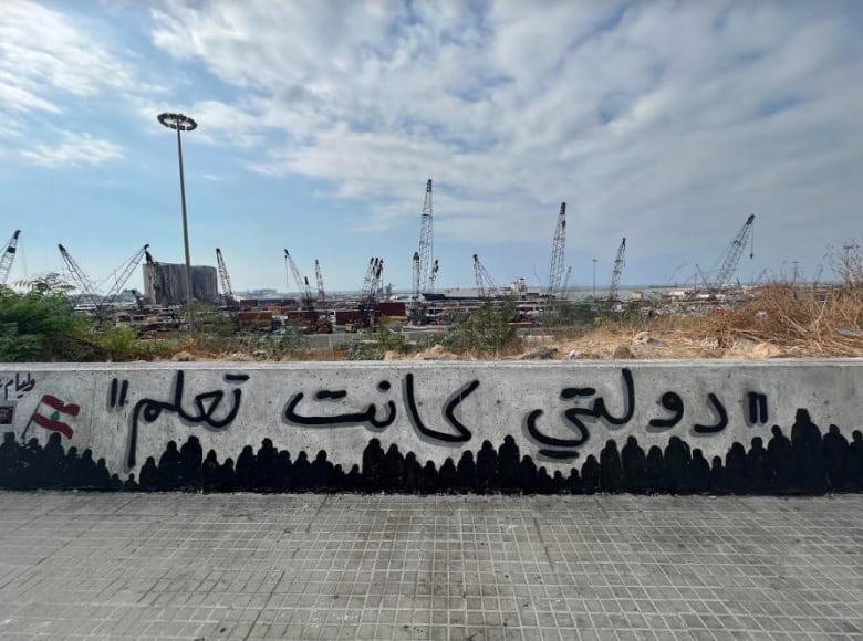 The damaged remains of the Beirut port with graffiti in Arabic saying “my country knew” on a wall surrounding the port lands.  