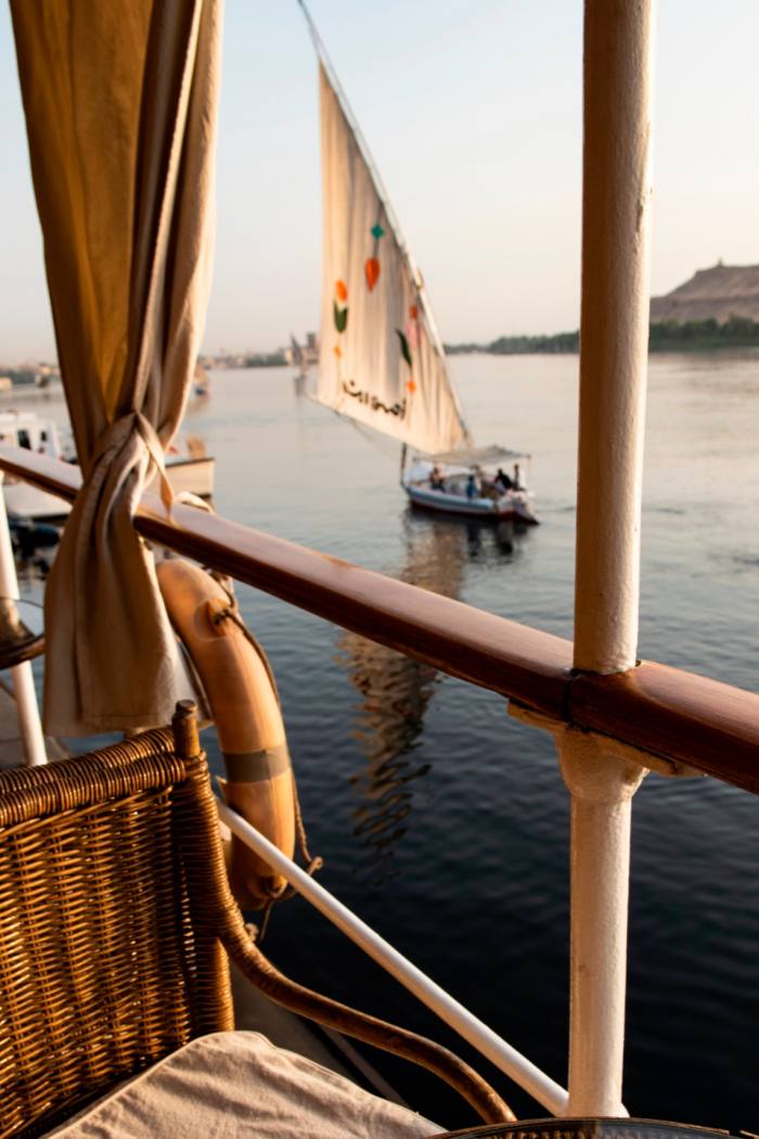 A wicker chair on the deck with a sailing boat on the water