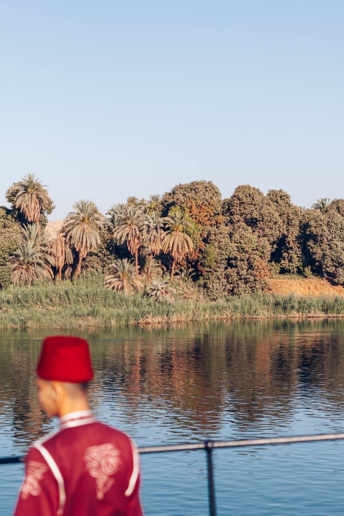 A man in red standing against a railing looks at the water