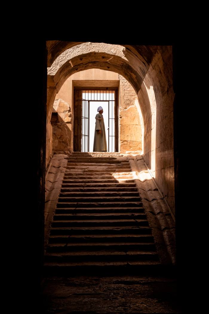 A man stands at the top of a staircase, in front of a window