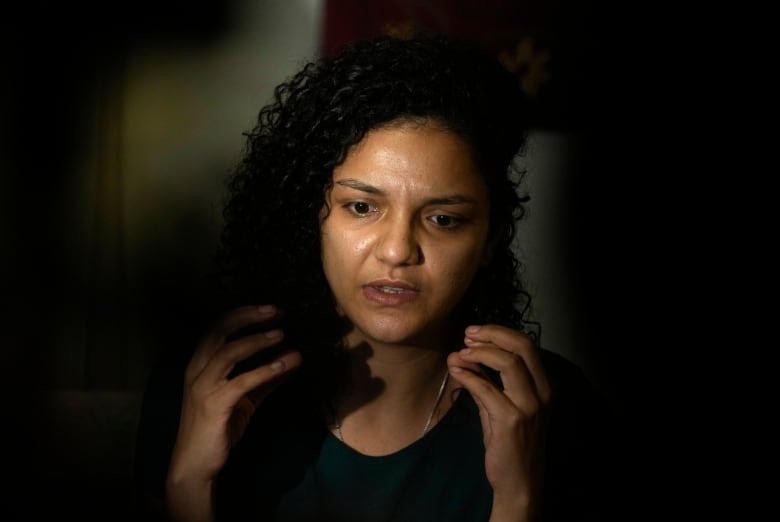 Individual with long, curly dark hair, gestures as she speaks. 