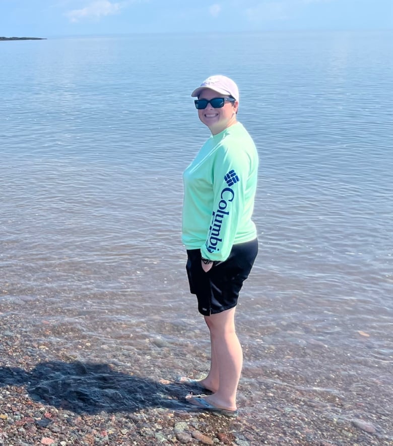 A woman wades on a rocky beach. 