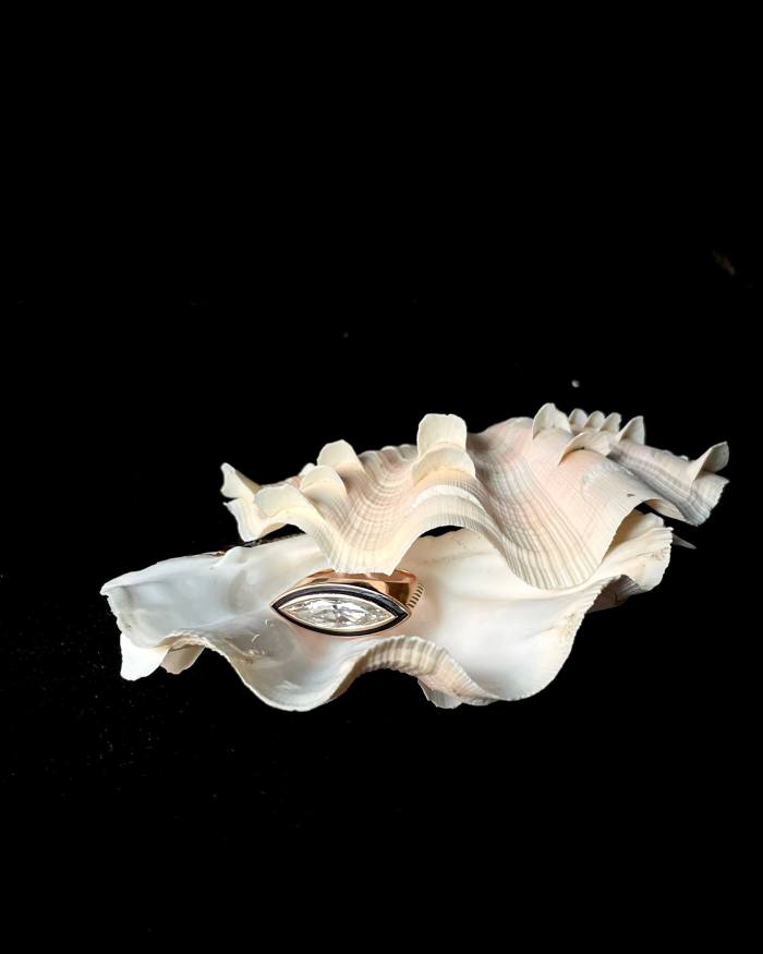 A Sara Beltrán diamond ring set in black enamelling pictured between two clam shells 