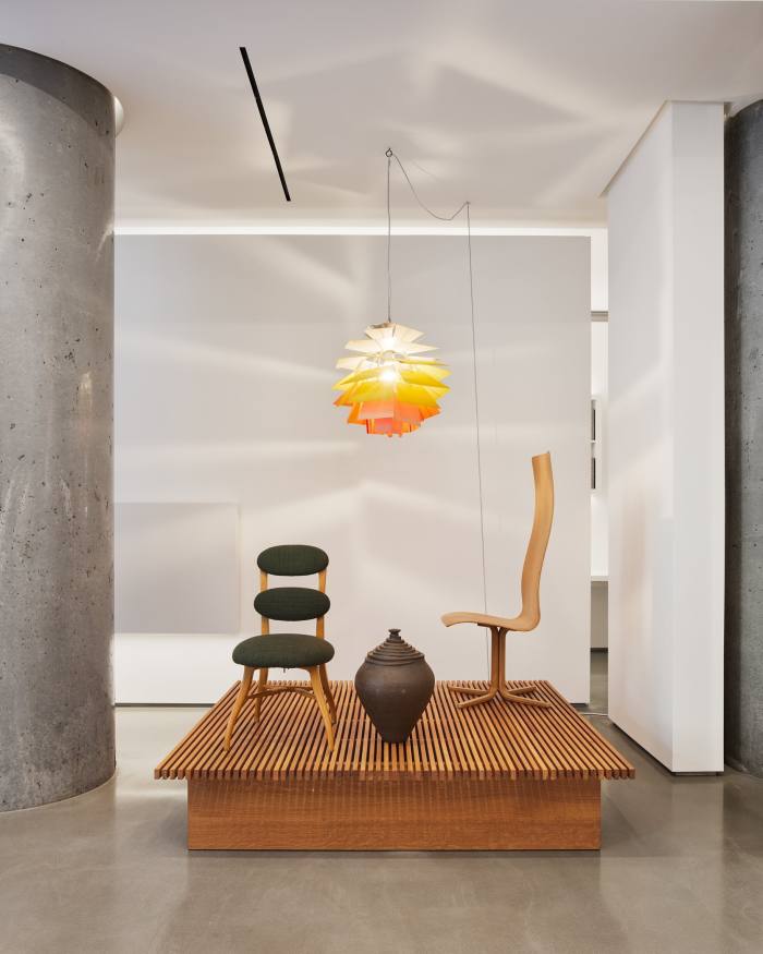 Two modernist chairs and an urn sitting on a platform beneath modernist lighting at Galerie56