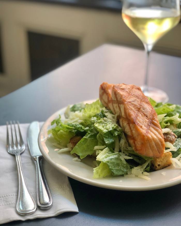 A plate of Caesar salad with salmon at Estancia 460, with a knife and fork to its left