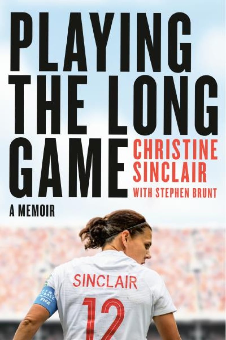 A female soccer player looks to her right with her back to camera. Her white jersey reads "Sinclair" with the number 12 on it in red text. In the background, out of focus, is a crowd of people wearing red and white seated in a soccer stadium. Above the woman, in the sky, the text of the book cover reads "Playing the Long Game" in black and the authors' names "Christine Sinclair with Stephen Brunt" in red. 