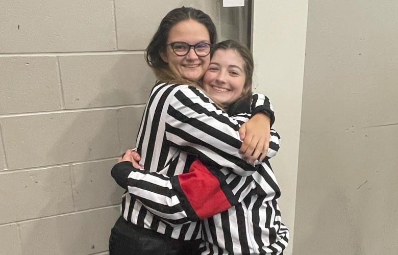 Two women in referee uniforms smiling. 