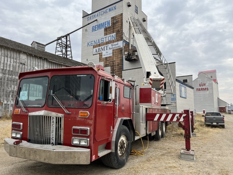 A fire ladder truck is parked in front of a grain elevator that is in the process of having its siding removed. 