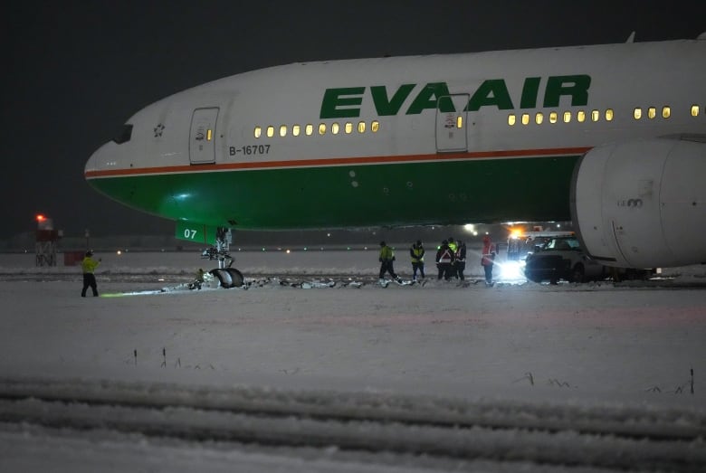 An Eva Air passenger jet pictured static in the snow off the side of an airport runway at night.