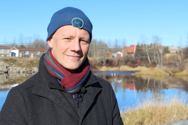 A man in a tuque and a striped scarf stands in front of a body of water