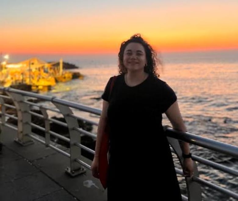 A smiling woman on a path overlooking the ocean as the sun sets.  