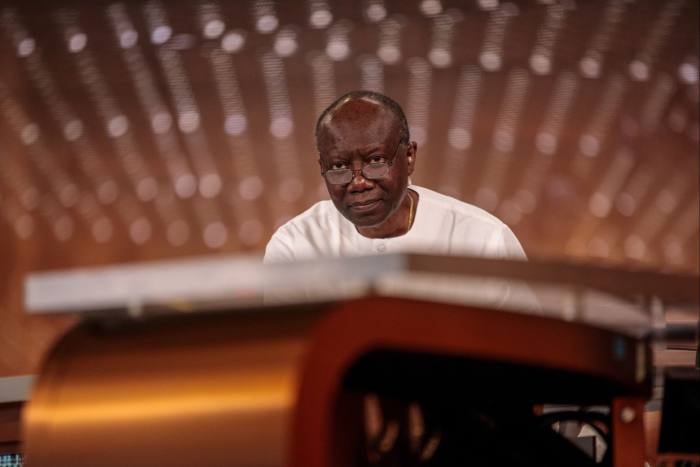 Ken Ofori-Atta, sitting alone, wearing glasses and a white shirt