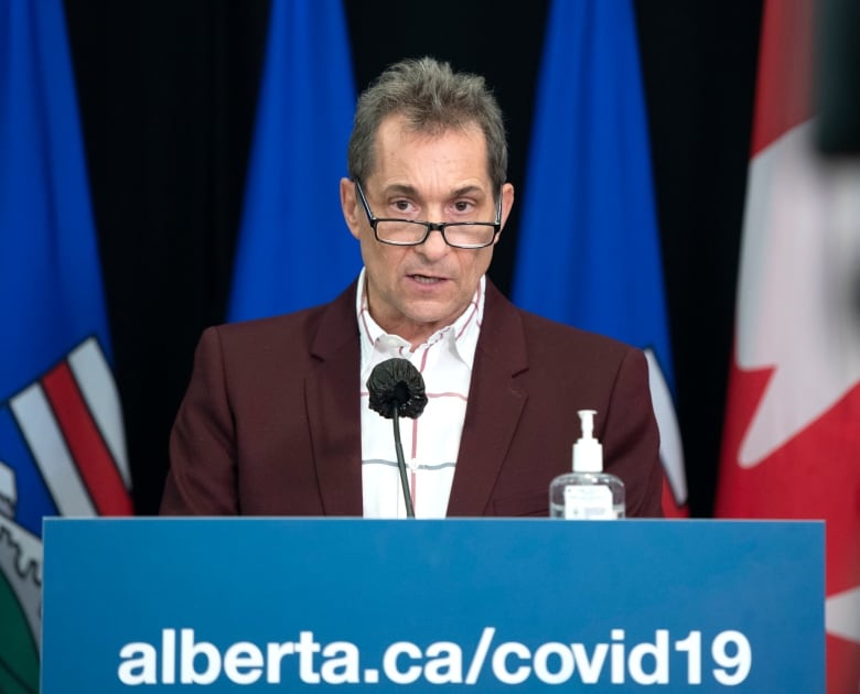 A man with spectacles stands behind a podium.