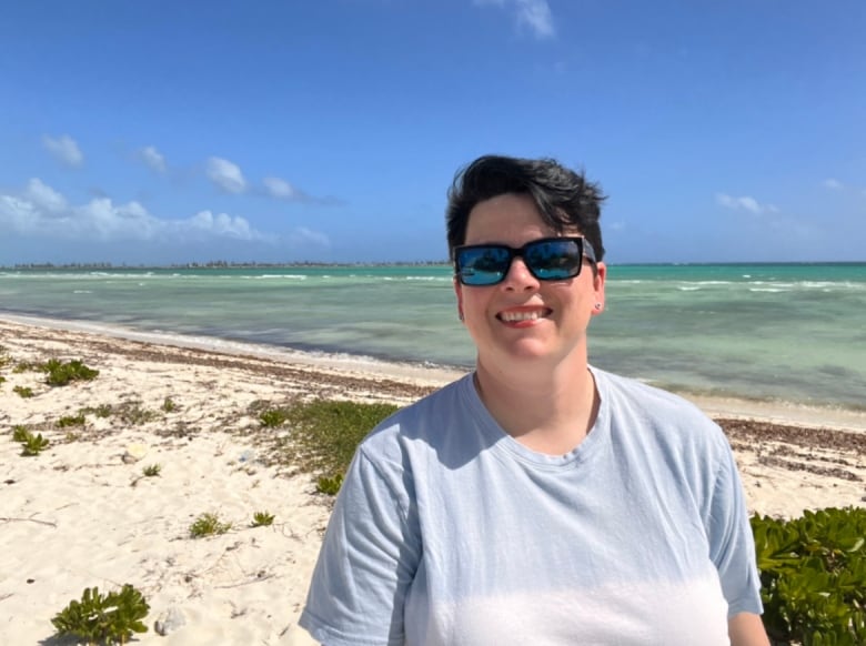 A smiling woman stands on a warm, sandy beach.  