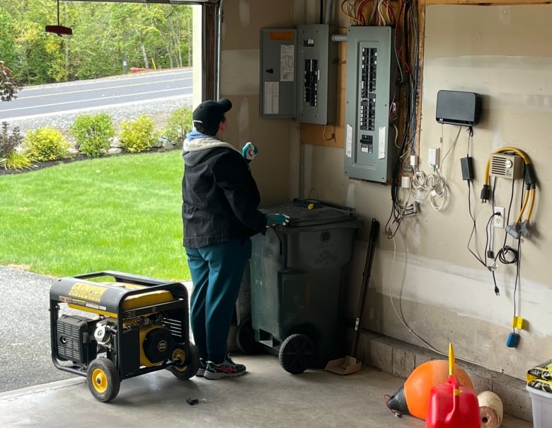 A woman stands next to a generator and breakers in a garage.