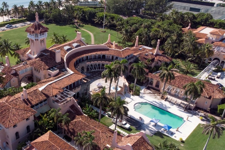 An aerial view of a posh resort surrounded by palm trees with a swimming pool at the centre.