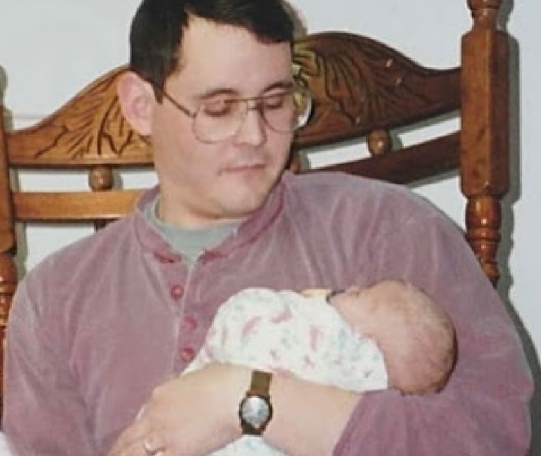 A man sitting in a chair holds a baby.