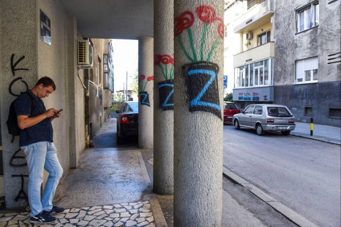 Man on his phone stands on a pavement with pillars