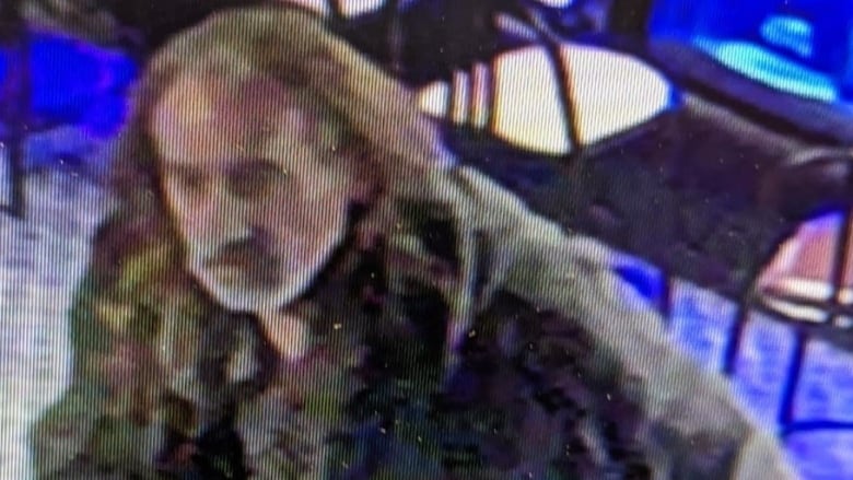 Surveillance camera photo of a man with a grey beard and camouflage jacket.