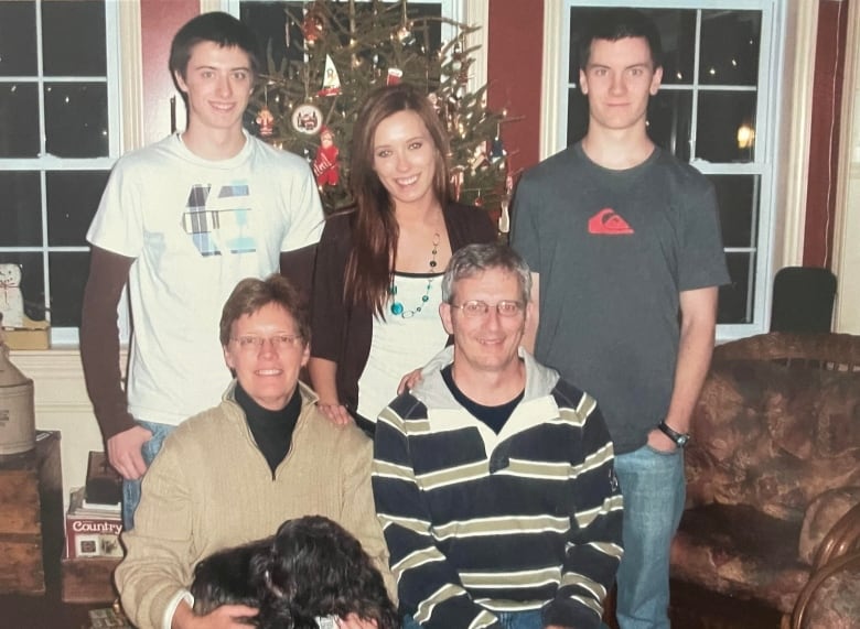 A portrait of a smiling family: A woman holds a dog in her lap while sitting next to a man. Three younger people stand behind them. 