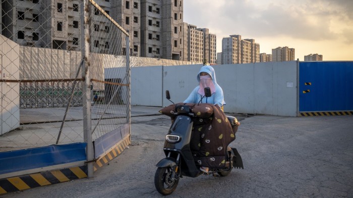 A woman rides a scooter past the China Evergrande Group Royal Peak development in Beijing