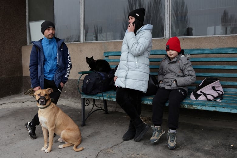 Parents waiting with their son and pets at a bus station. 