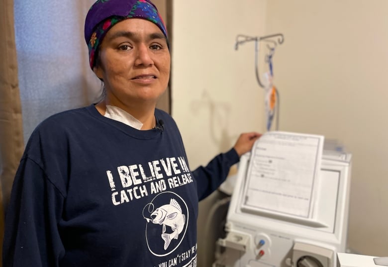 A woman stands in front of her dialysis machine in a room on Windigo Island.