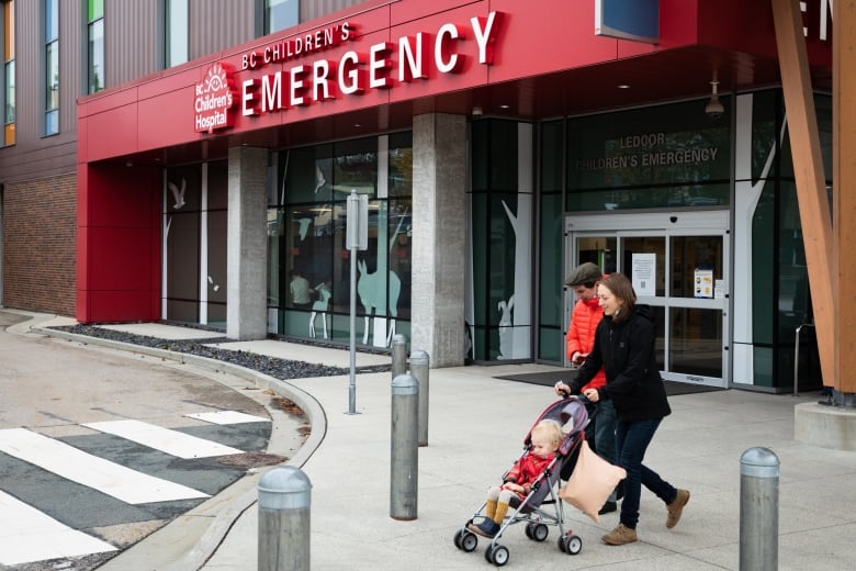 A couple with a stroller walk in front of BC Children’s Hospital Emergency Department.