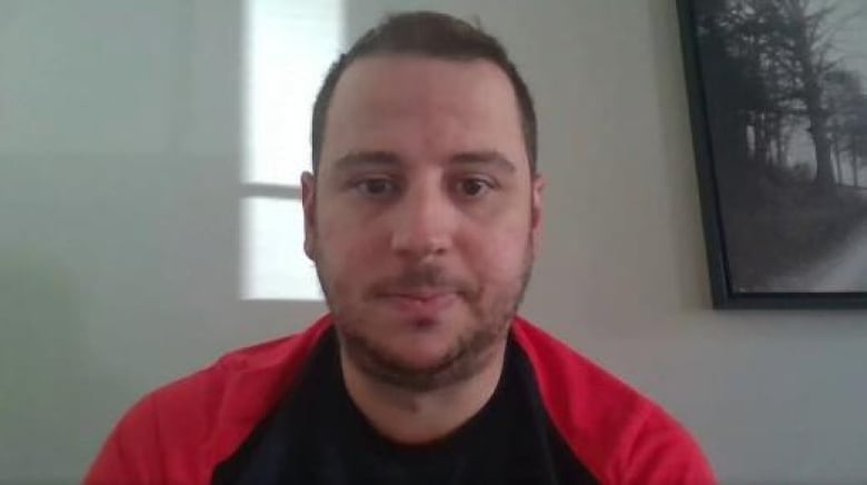 Man with short hair wearing red and black shirt.