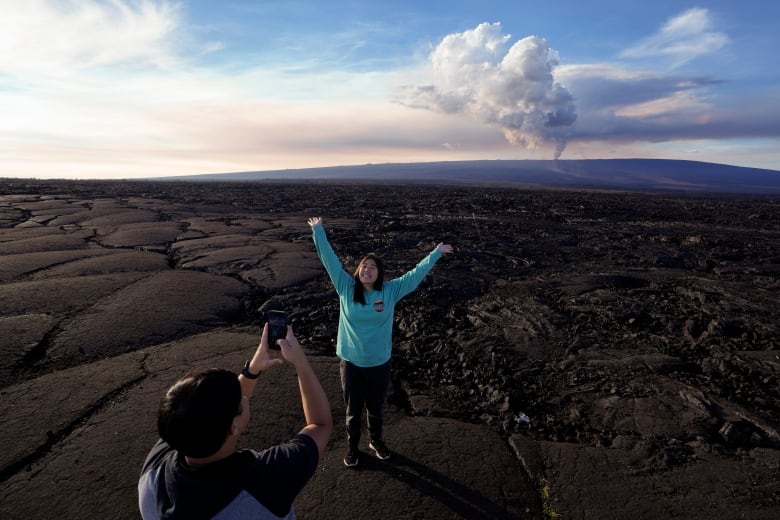 A young person smiles with her arms up in the air with the volcano in the distance. 